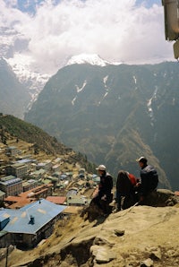 a group of people sitting on a cliff overlooking a mountain