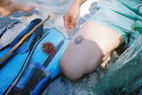 a woman sitting on the sand with a tattoo on her arm