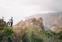 two people standing on a cliff overlooking the ocean