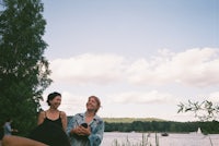 two women sitting on the shore of a lake
