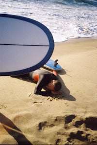 a man laying on the sand next to a surfboard