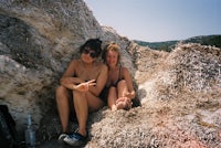 two women sitting on top of a large rock