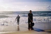 two people walking on the beach with surfboards
